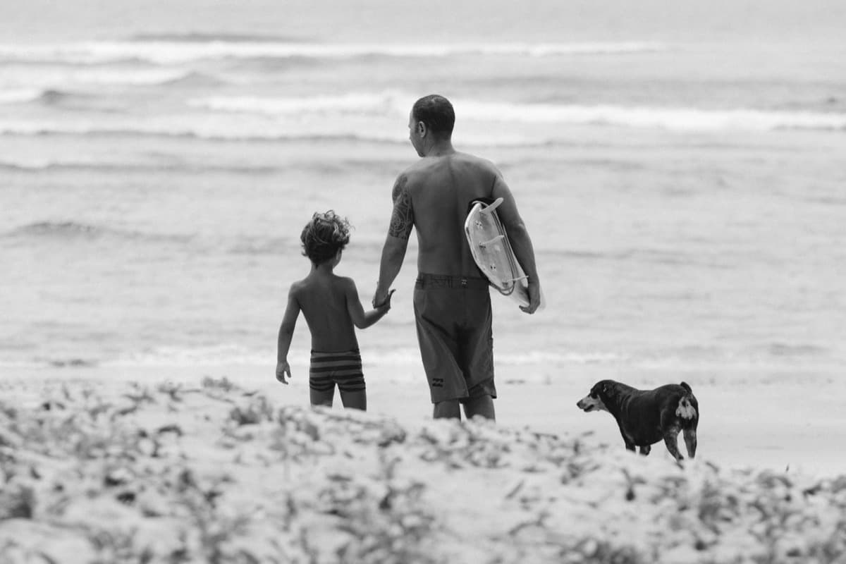 Family with dog and surfboard walking on Lisbon beach